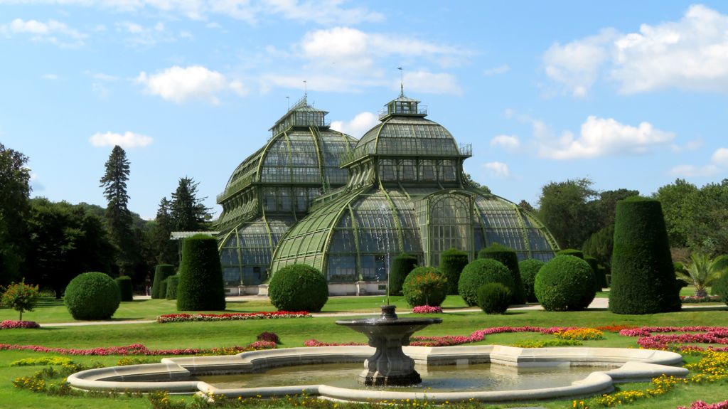 Ornate glasshouse with lush gardens at Schönbrunn Palace on a sunny day.